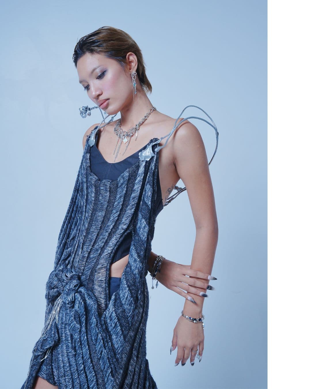 Person in a textured blue knit dress with metallic wire shoulder pieces and silver jewelry.