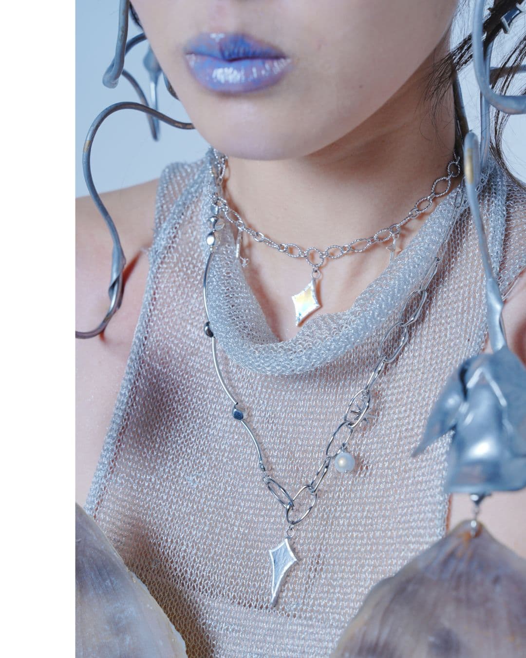 Person with blue glossy lips wearing layered silver necklaces and a shimmering mesh top.