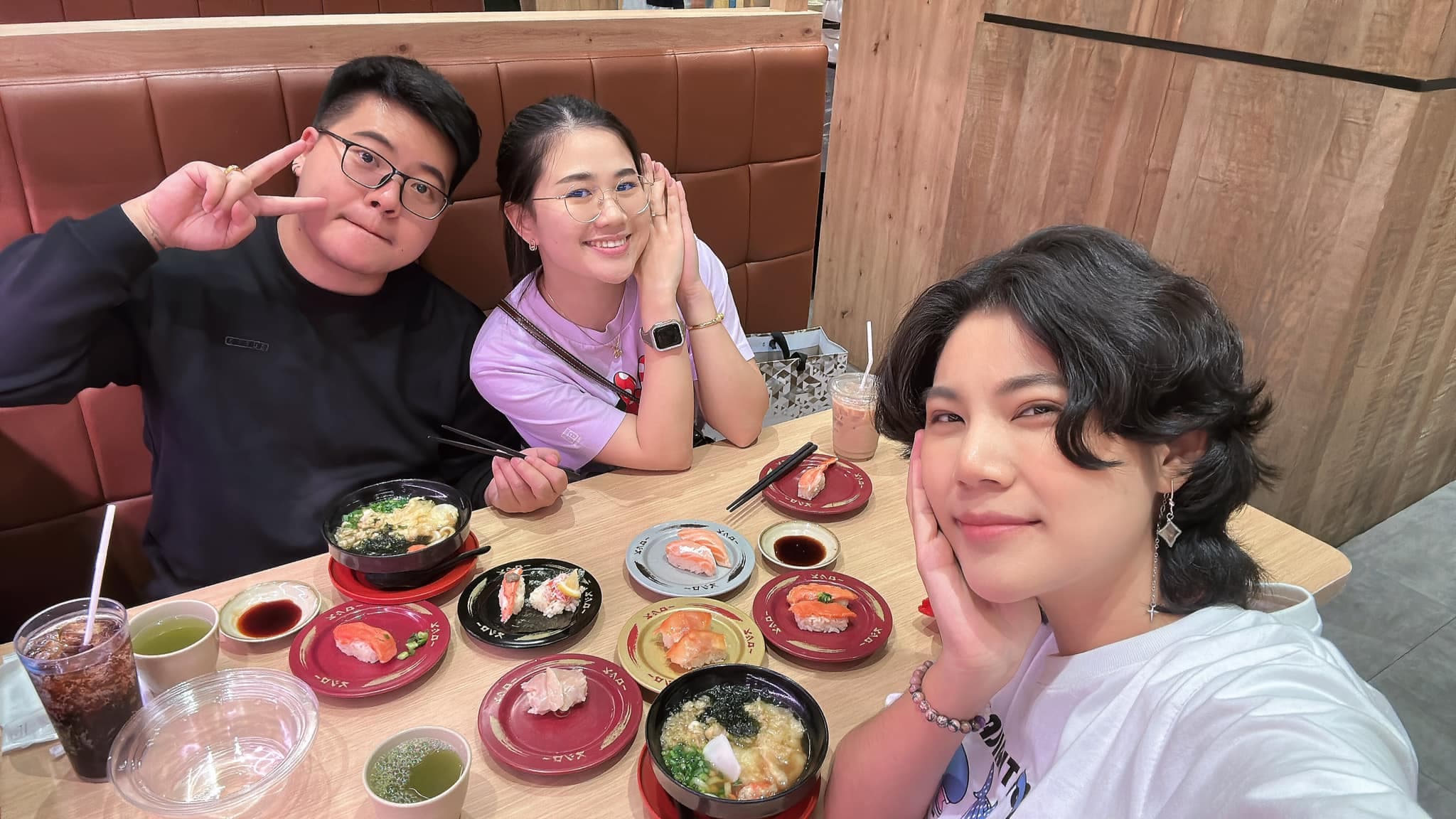 Three friends posing for a selfie at a restaurant table filled with sushi and ramen.
