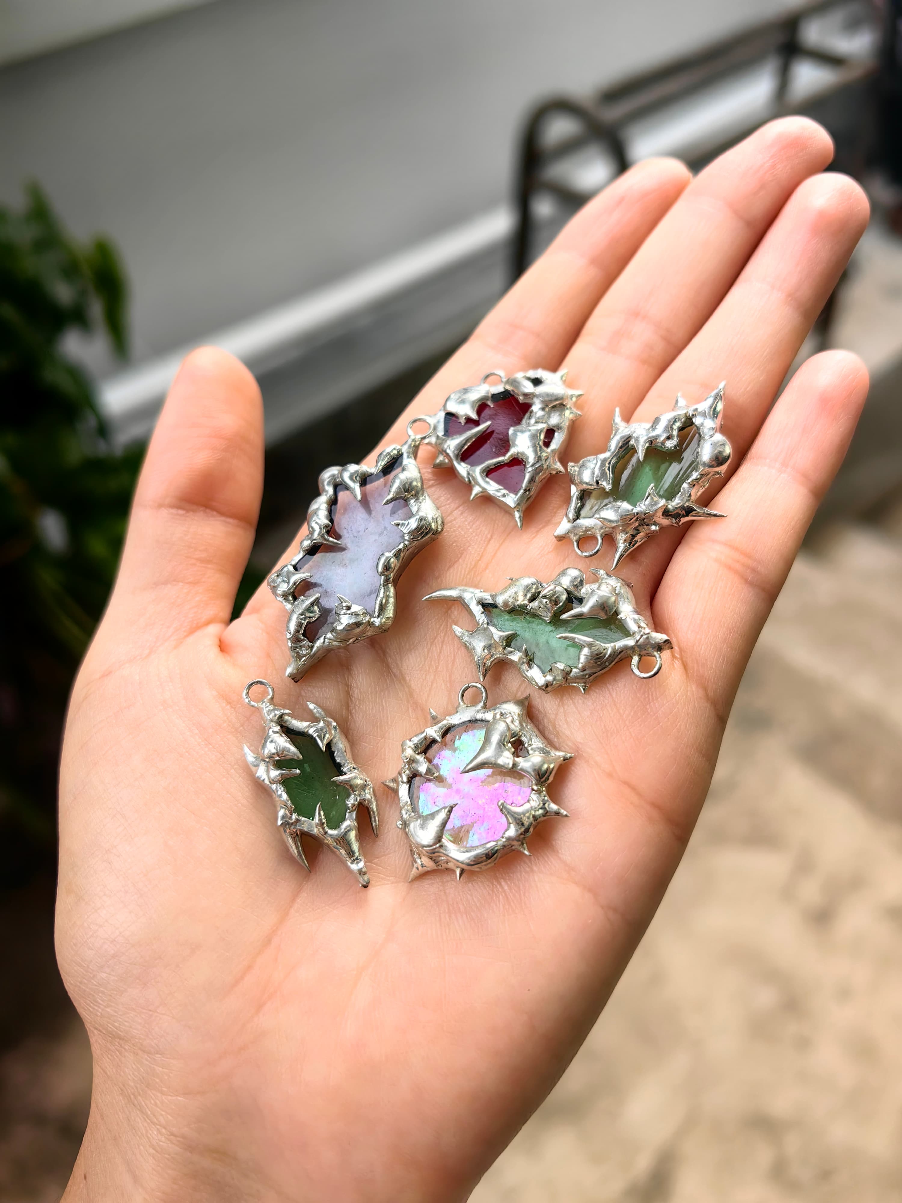 Six handcrafted silver pendants with sharp, thorn-like settings and colorful stones in an open palm.