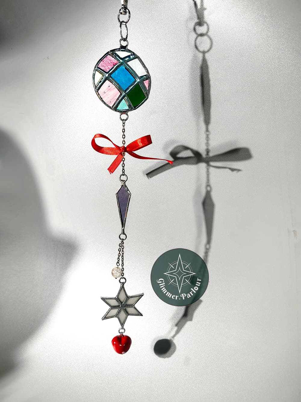 Stained glass suncatcher with colorful geometric shapes, a red bow, star, and heart charm.